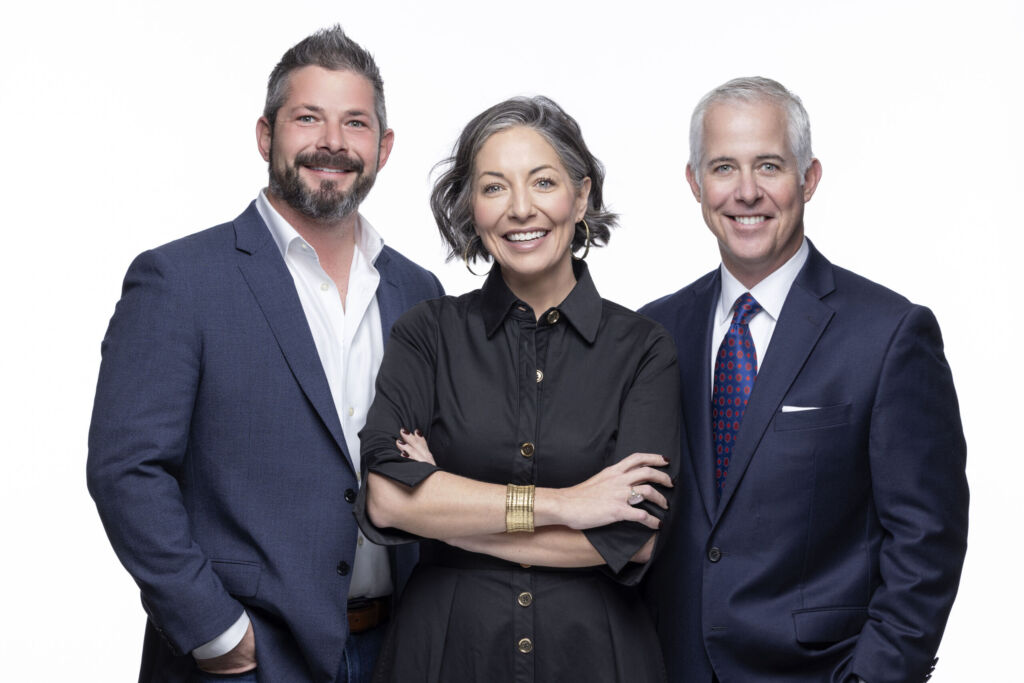 Portrait of three smiling Antique Brick & Block team members in navy suits and a black dress against a white background