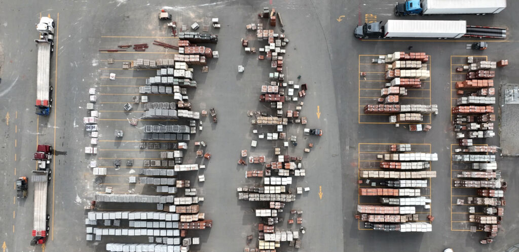 Aerial view of an outdoor masonry yard with rows of palletized brick, block, and stone beside parked semi trailers
