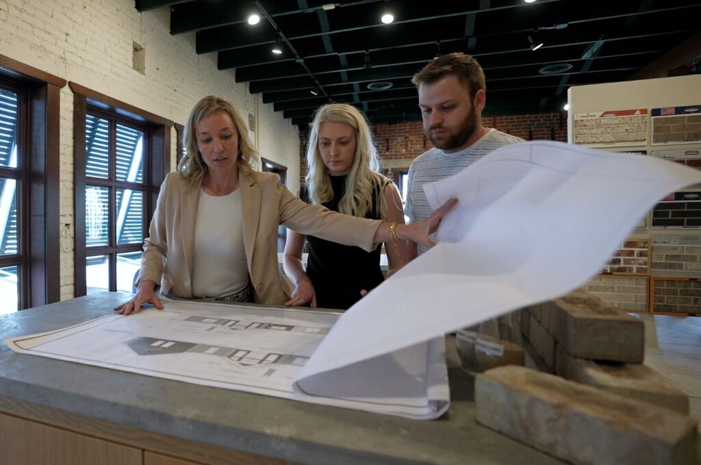 Three staff members reviewing building plans on a counter in a brick and stone product showroom