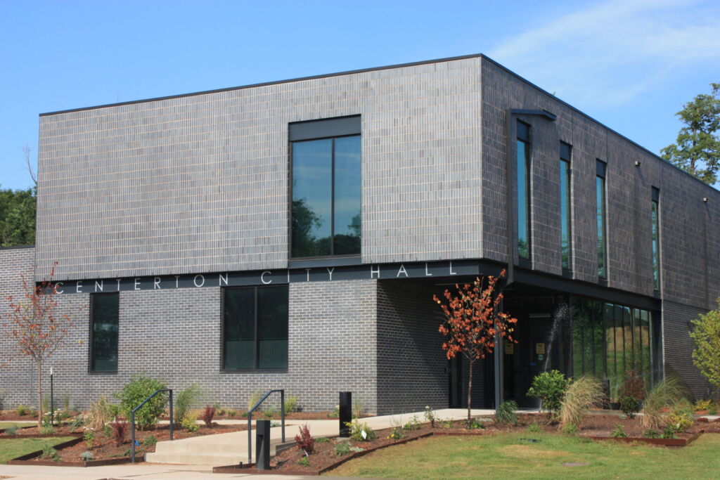 Centerton City Hall building clad in gray and charcoal brick with large windows and landscaped entry under a blue sky