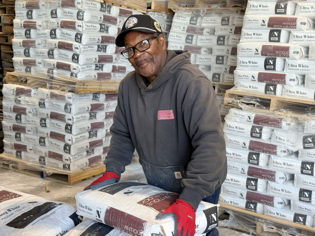 Antique Brick & Block worker in a ball cap stacking bags of Ultra White masonry cement on pallets in the yard