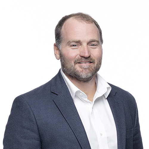 Portrait of Adam McPike, Antique Brick & Block team member, smiling in a navy blazer