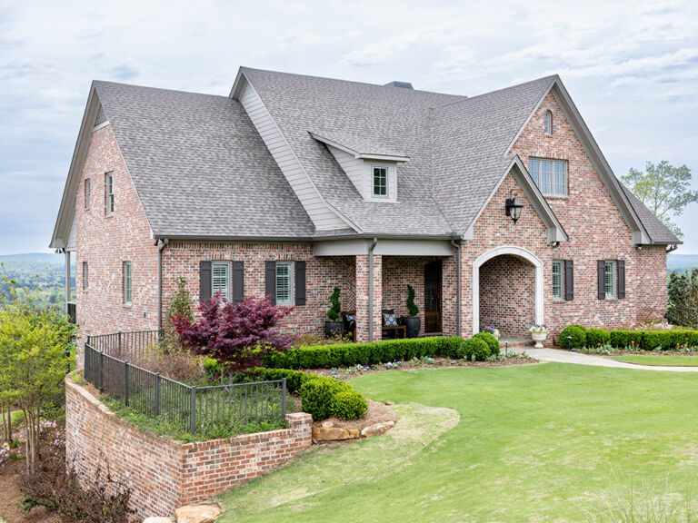 Large two-story pink-tan brick home with arched entry, dark shutters, and manicured lawn