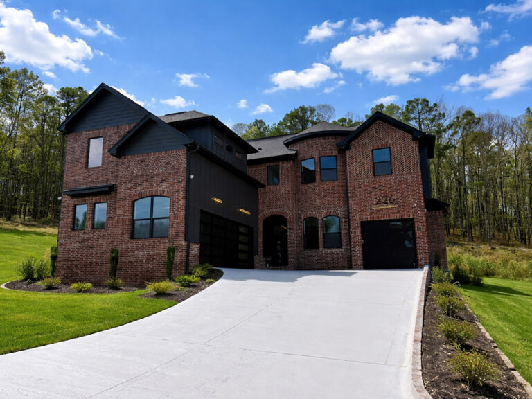 Two-story dark red brick home with black board-and-batten accents, arched garage, and manicured green lawn